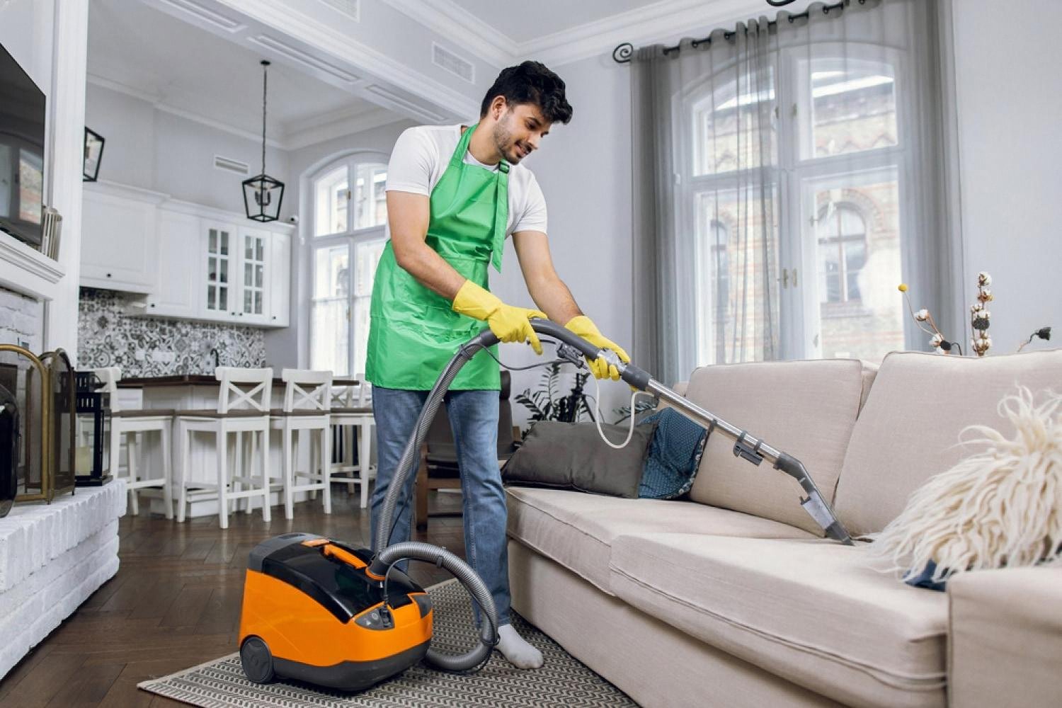 Professional cleaner using a heavy-duty vacuum to deep clean a beige sofa in a UAE living room